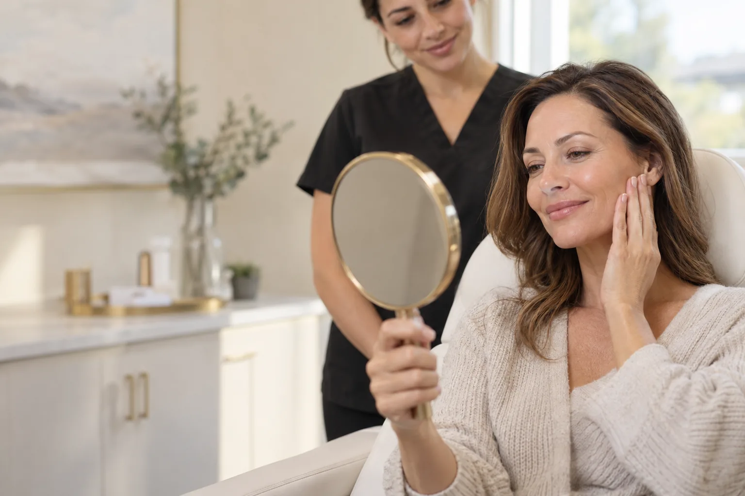 A woman smiling at her reflection in a hand mirror after her treatment